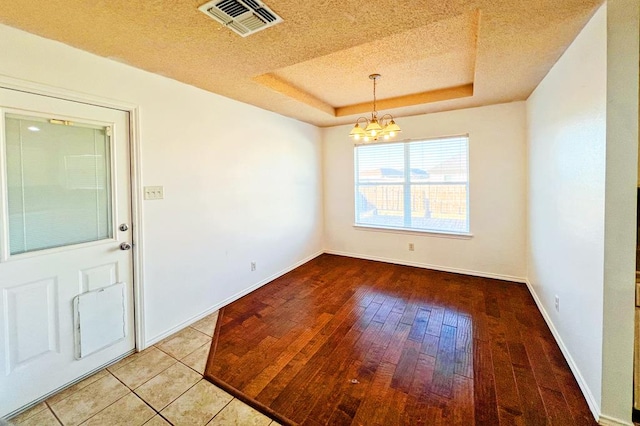 unfurnished dining area with visible vents, a tray ceiling, a textured ceiling, wood-type flooring, and a chandelier