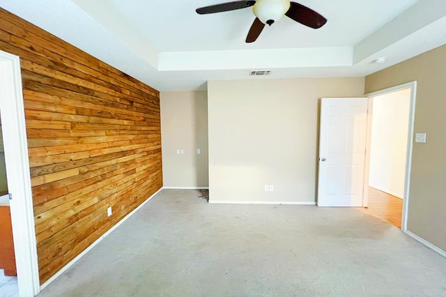 empty room with visible vents, wood walls, baseboards, and a tray ceiling