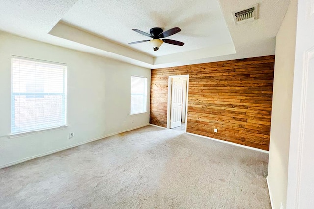 unfurnished room with visible vents, a raised ceiling, wooden walls, and a textured ceiling