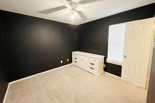 spare room with light colored carpet, a textured ceiling, baseboards, and a ceiling fan