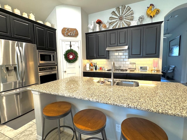 kitchen featuring a kitchen island with sink, light stone countertops, decorative backsplash, and stainless steel appliances