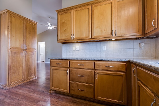 kitchen featuring dark wood-type flooring, lofted ceiling, ceiling fan, light stone countertops, and decorative backsplash