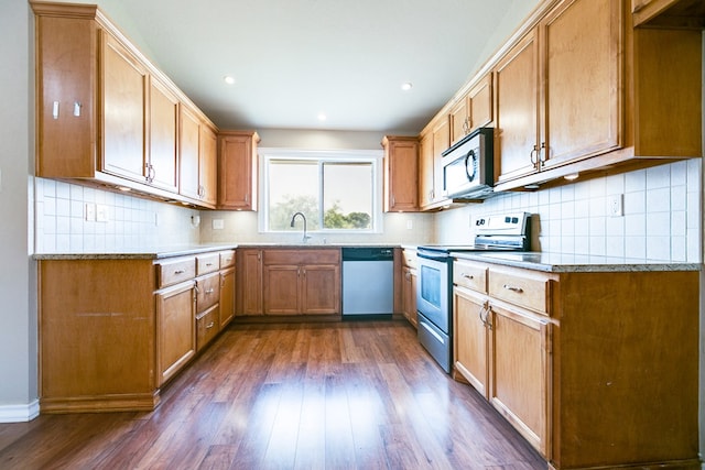 kitchen featuring sink, light stone counters, dark hardwood / wood-style flooring, stainless steel appliances, and backsplash