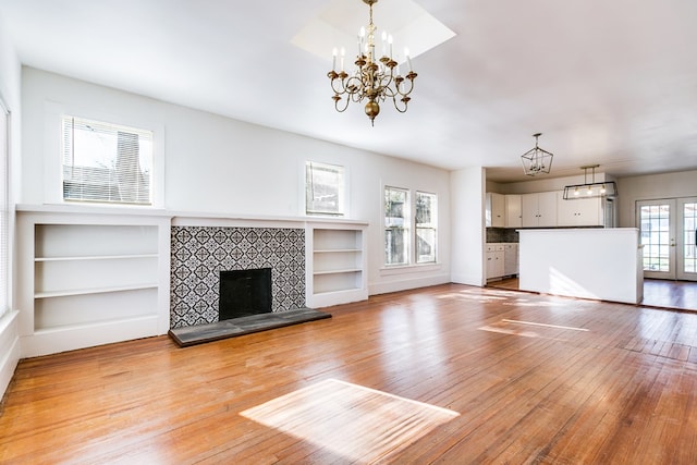 unfurnished living room with french doors, a tile fireplace, light hardwood / wood-style flooring, and a notable chandelier