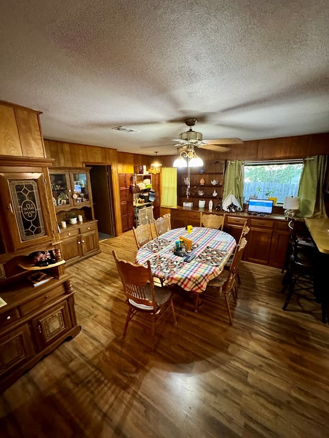 dining area with ceiling fan, a textured ceiling, wooden walls, and wood-type flooring