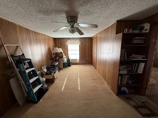 miscellaneous room featuring ceiling fan, a textured ceiling, wooden walls, and light colored carpet