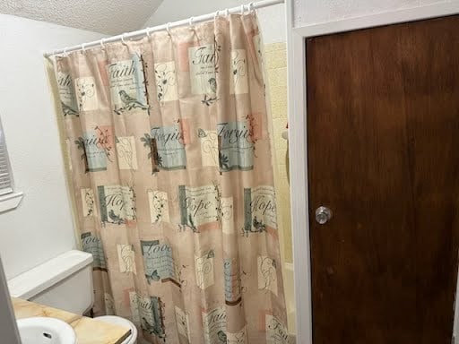 bathroom featuring lofted ceiling, a textured ceiling, toilet, and shower / bath combination with curtain