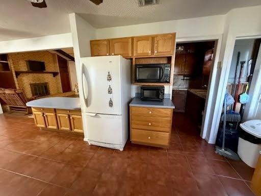 kitchen with white fridge, a textured ceiling, black microwave, a fireplace, and dark tile patterned floors