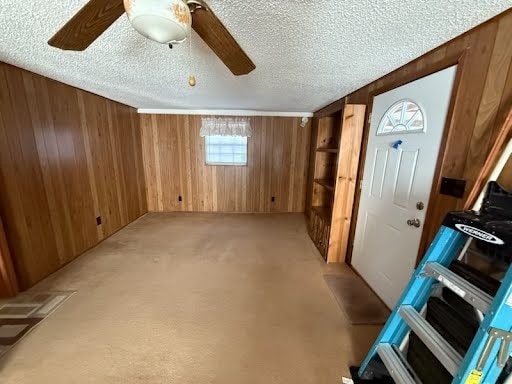 interior space with ceiling fan, a textured ceiling, light colored carpet, and wooden walls