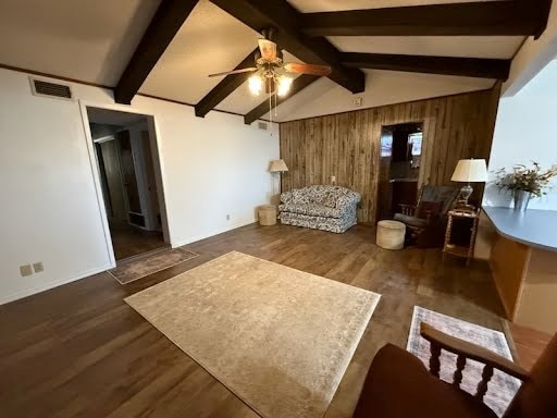 living room featuring dark wood-type flooring, vaulted ceiling with beams, wood walls, and ceiling fan