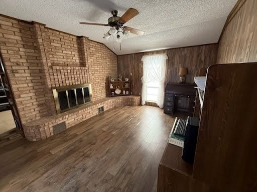 unfurnished living room featuring a brick fireplace, vaulted ceiling, wood-type flooring, wood walls, and a textured ceiling