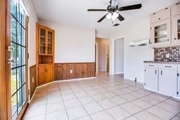 1246 E 20th St, San Angelo, TX 76903 - kitchen featuring white cabinets, light tile patterned floors, wainscoting, ceiling fan, and glass insert cabinets