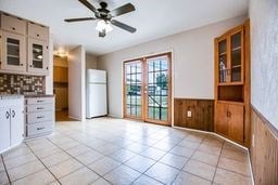 1246 E 20th St, San Angelo, TX 76903 - kitchen featuring ceiling fan, freestanding refrigerator, a wainscoted wall, light tile patterned flooring, and glass insert cabinets