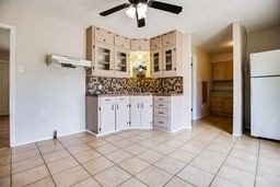 1246 E 20th St, San Angelo, TX 76903 - kitchen with freestanding refrigerator, ceiling fan, light tile patterned floors, tasteful backsplash, and glass insert cabinets