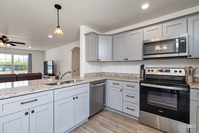 kitchen with gray cabinets, appliances with stainless steel finishes, decorative light fixtures, sink, and light stone counters