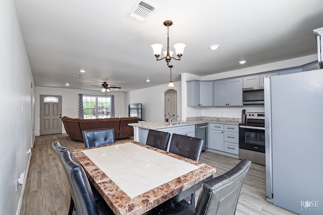 kitchen featuring ceiling fan with notable chandelier, sink, hanging light fixtures, stainless steel appliances, and light hardwood / wood-style flooring