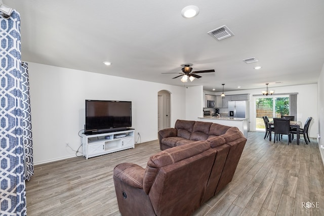 living room featuring ceiling fan with notable chandelier and light hardwood / wood-style floors