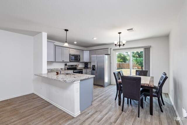 kitchen featuring gray cabinets, appliances with stainless steel finishes, decorative light fixtures, kitchen peninsula, and a chandelier