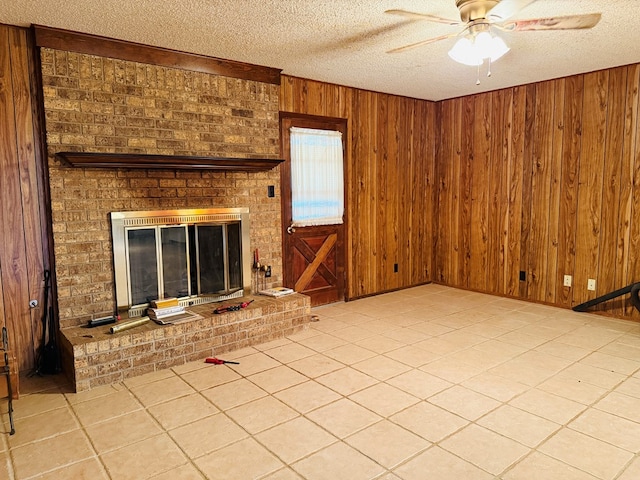 unfurnished living room featuring a fireplace, wood walls, light tile patterned floors, ceiling fan, and a textured ceiling