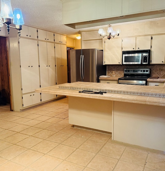 kitchen with tile countertops, hanging light fixtures, a textured ceiling, appliances with stainless steel finishes, and decorative backsplash