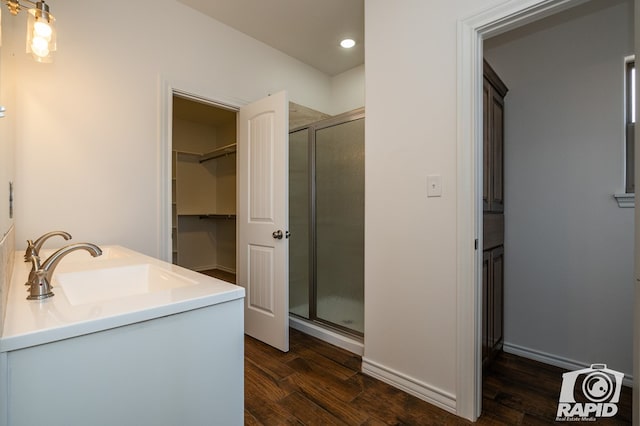 full bathroom with a spacious closet, a sink, a shower stall, wood finished floors, and baseboards