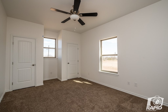 unfurnished bedroom with ceiling fan, multiple windows, baseboards, and dark colored carpet