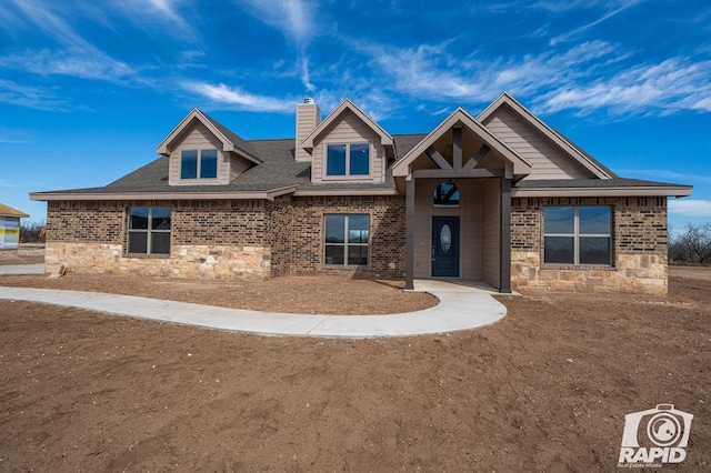 craftsman inspired home with a shingled roof, stone siding, brick siding, and a chimney