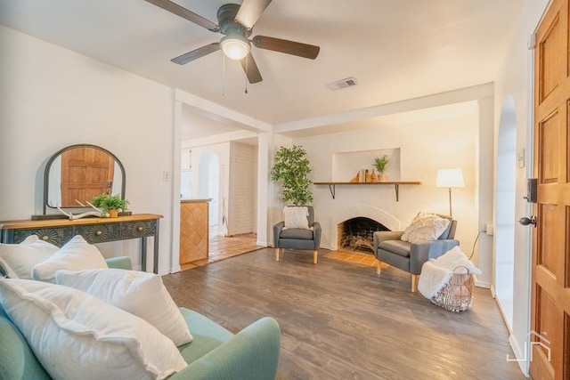 living room with a ceiling fan, wood finished floors, visible vents, and a fireplace