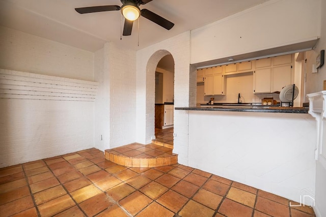 interior space featuring dark countertops, cream cabinets, arched walkways, brick wall, and ceiling fan