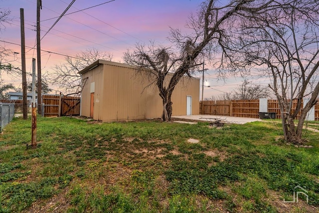 yard at dusk featuring an outdoor structure, a fenced backyard, and a patio