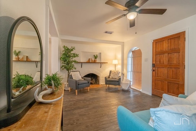 living room with a fireplace, wood finished floors, visible vents, and ceiling fan