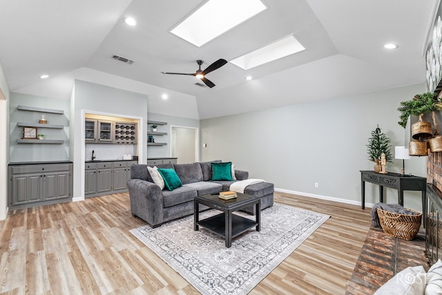 living room with ceiling fan, built in features, vaulted ceiling with skylight, and light hardwood / wood-style flooring