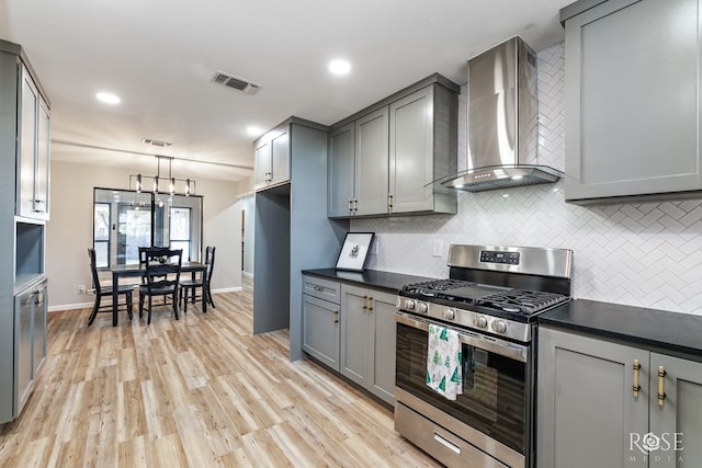 kitchen featuring gray cabinetry, gas range, pendant lighting, and wall chimney exhaust hood