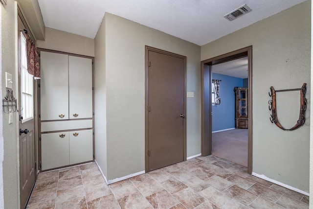 hallway featuring stone finish floor, baseboards, visible vents, and a textured ceiling