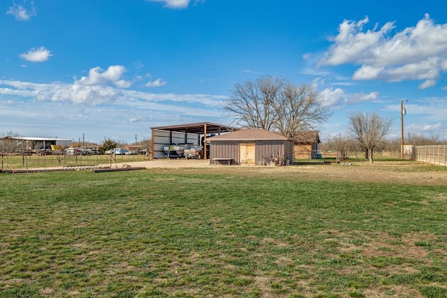 view of yard featuring a rural view, fence, a carport, and an outbuilding