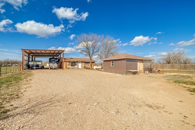 rear view of property featuring driveway, a pole building, fence, an outdoor structure, and a detached carport