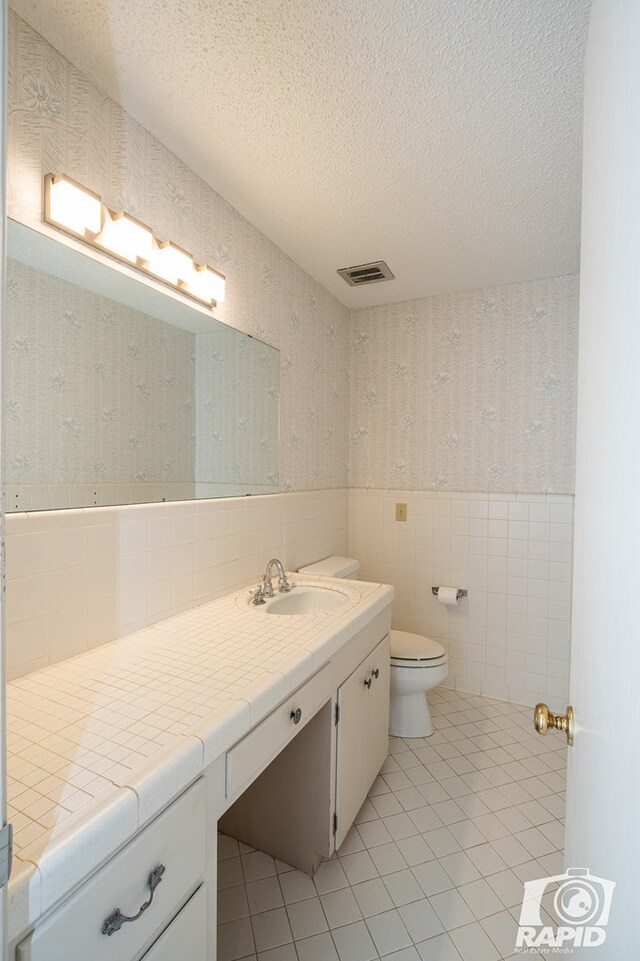 bathroom with tile patterned floors, vanity, tile walls, and a textured ceiling