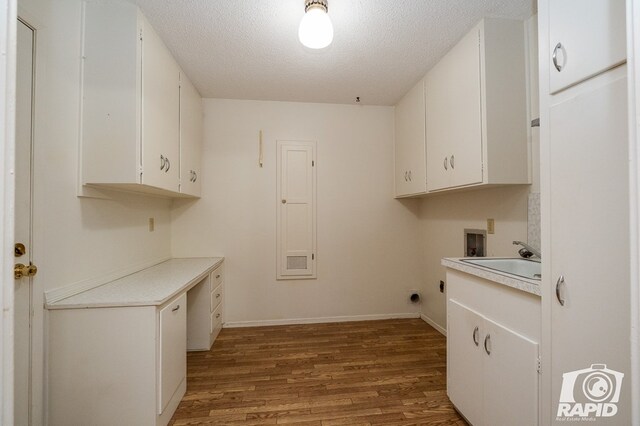 clothes washing area with sink, cabinets, wood-type flooring, a textured ceiling, and washer hookup