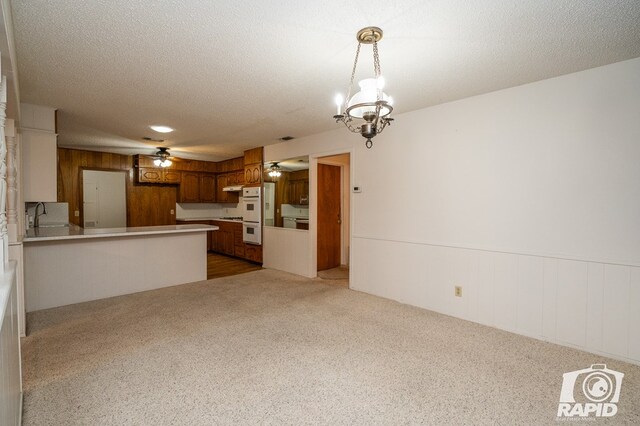 unfurnished living room with ceiling fan with notable chandelier, sink, carpet floors, and wood walls