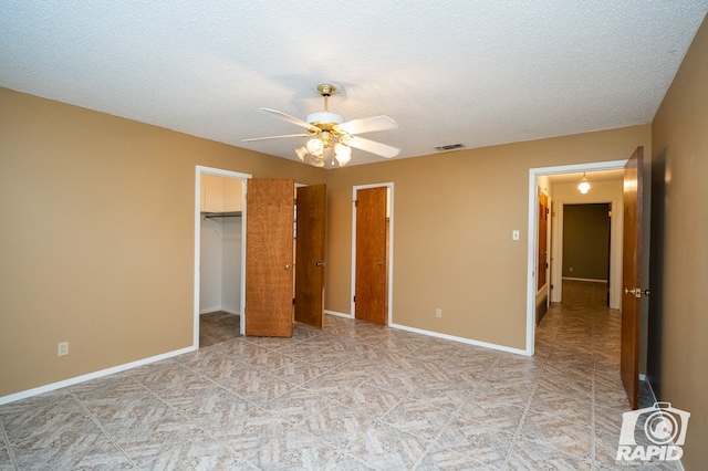 unfurnished bedroom with ceiling fan, a spacious closet, and a textured ceiling