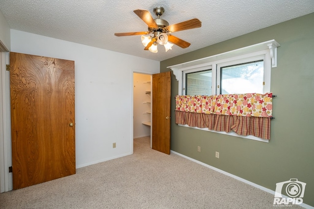 unfurnished bedroom with light carpet, a textured ceiling, ceiling fan, and a spacious closet