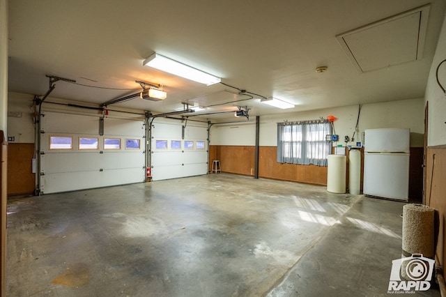 garage featuring white refrigerator, a garage door opener, and wooden walls