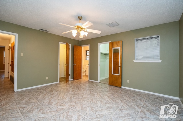 unfurnished bedroom featuring a textured ceiling, a walk in closet, a closet, and ceiling fan