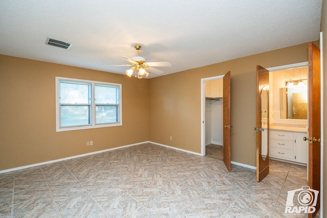 unfurnished bedroom with ensuite bathroom, a spacious closet, ceiling fan, a textured ceiling, and a closet