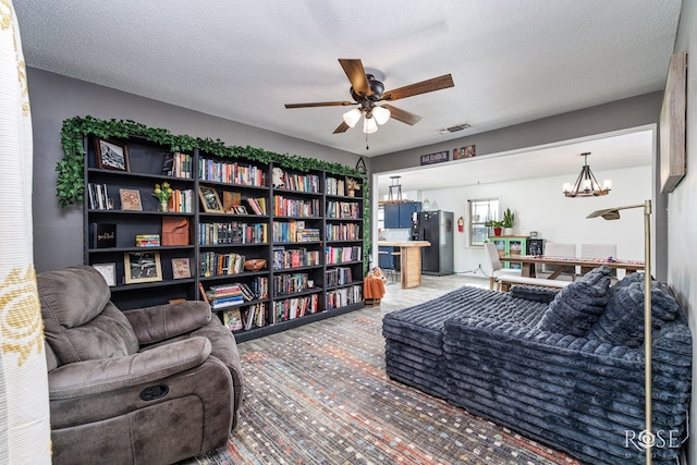 living room featuring ceiling fan with notable chandelier and a textured ceiling