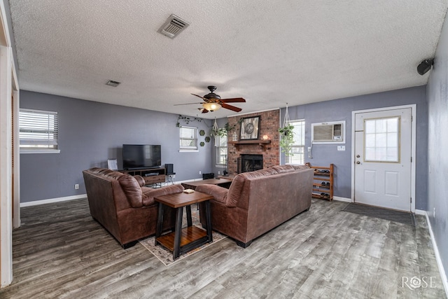 living room featuring wood-type flooring, a brick fireplace, a wall mounted AC, and ceiling fan