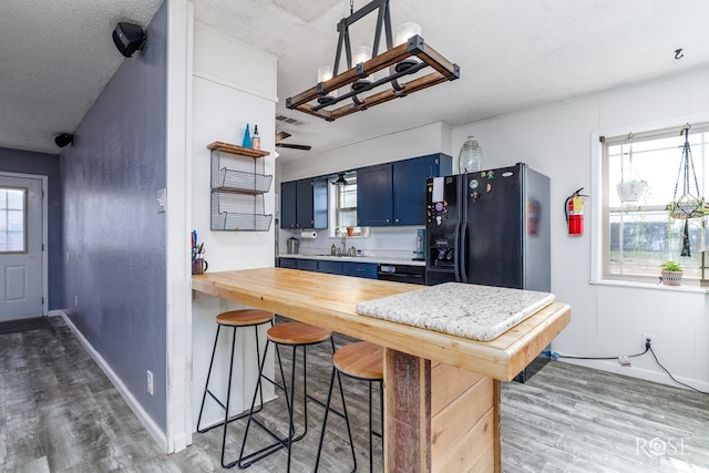 kitchen with sink, black fridge with ice dispenser, blue cabinetry, and dark hardwood / wood-style floors