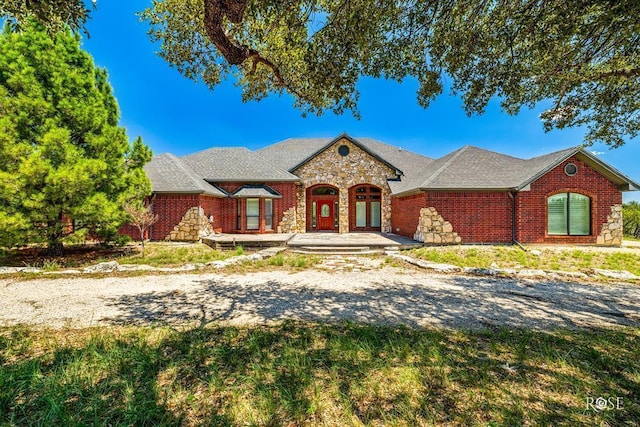 view of front of home featuring stone siding, a shingled roof, and brick siding