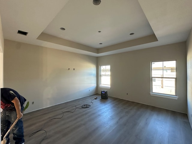 empty room with a raised ceiling, wood finished floors, and visible vents