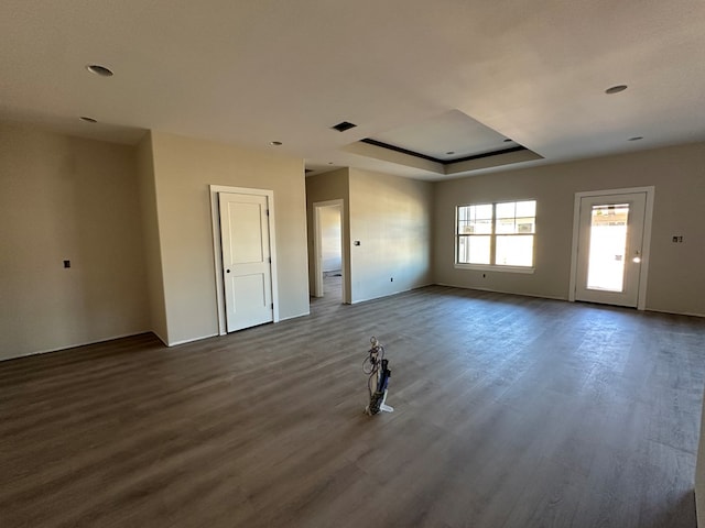 spare room with a tray ceiling, visible vents, and dark wood-style floors